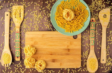 fettuccine pasta on a green plate and on a bamboo cutting Board and a spoon with pasta on a wooden background