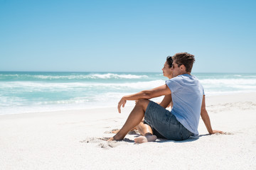 Fototapeta na wymiar Contemplative young couple sitting on white beach