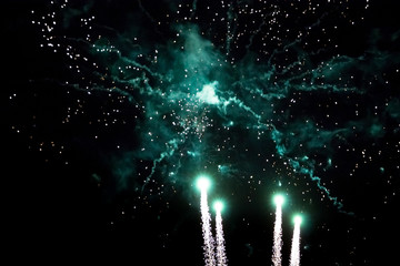 Green and aquamarine firework sparkles with beautiful smoke on black background during a holiday in the evening