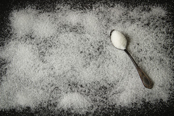 white sugar on a black background with a spoon of sugar