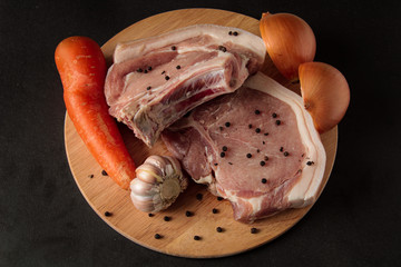 Raw pork chops on a cutting board, with vegetables, peppers, carrots, garlic, chopped onions