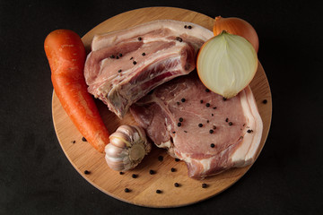 slices of strictly pork steak with vegetables, peppers, carrots, chopped onions, on a wooden board and black background