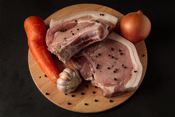 Meat. Raw pieces of pork with and pepper, carrots, garlic, onions. on a wooden board on a black background
