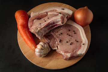 meat, pork sprinkled with pepper, with vegetables, onions, carrots and garlic, raw meat, on a wooden board and black background