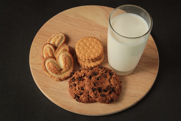 chocolate chip cookies and glass of milk, on a wooden board