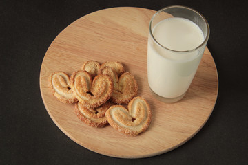glass of milk and cookies in the form of hearts, on a wooden board