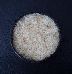 A bowl of raw long grain rice against a black background