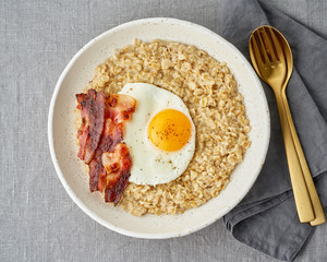Oatmeal, fried egg and fried bacon. Hearty fat high-calorie breakfast, source of energy.