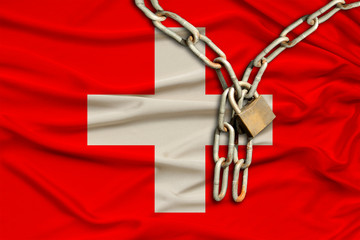 iron chain and lock on the silk national flag of Switzerland with beautiful folds, the concept of a...