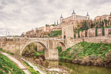 Fototapeta na wymiar Cityscape of Toledo in Spain with Tagus River and Roman bridge Puente de Alcantara. Famous UNESCO World Heritage Site. The historic city in hdr art photography.