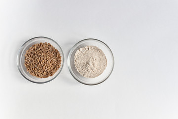 spelt grain seeds heap in glass bowl and powder  on white background