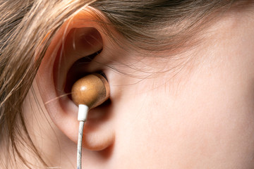 Wooden earphone inserted in the ear of a teenage girl close up