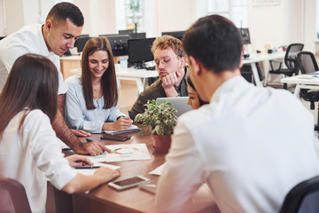 Young business people sitting by the table, talking and working together in the modern office