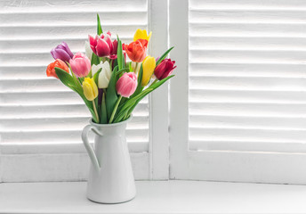 Bouquet with multicolored tulips on a window with wooden shutters on a light background