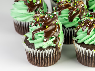 Chocolate cupcakes with green mint frosting and chocolate drizzle with sprinkles for St. Patrick’s Day on a white background!  Delicious and festive for the Irish holiday!