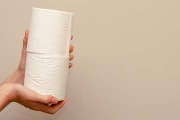 Close up of hands holding two toilet paper rolls on neutral background. Shortage and stockpile concept