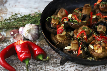 Selective focus. Large baked champignons in a pan with herbs and chili peppers. Vegan lunch recipe idea.