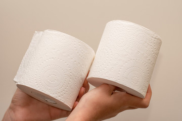 Close up of hands holding two toilet paper rolls on neutral background. Shortage and stockpile concept