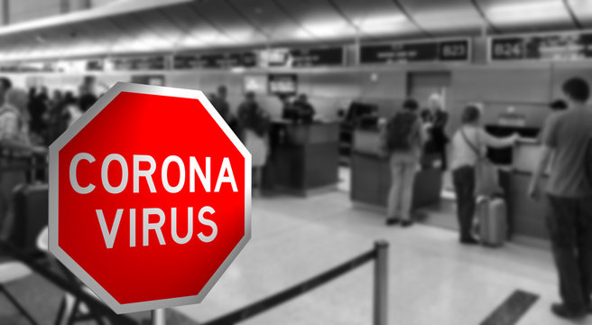 People crowd at airport check in desk with Corona Virus Sign