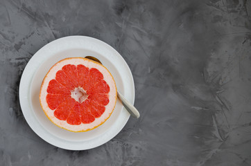 Fresh ripe juicy half of the grapefruit on a plate with a spoon on a dark concrete background. Healthy snack. Horizontal orientation. Copy space.