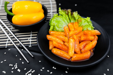 Spicy Tteokbokki on black crockery with metal chopstics.