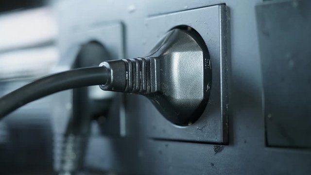 Hand of caucasian man plugs two black power plugs into black power sockets. ECU
