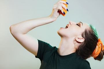 beautiful stylish girl threw head back and squeezes a drop of juice from half an orange into her...