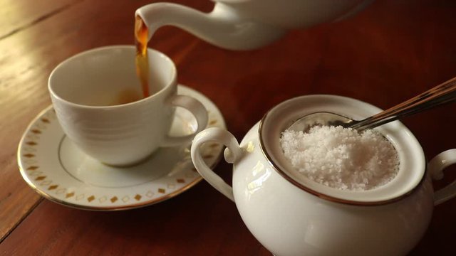 cup of tea pouring into a tea glass with sugar on wood table. closeup footage video clip