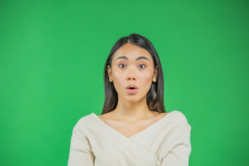 Obraz premium Surprise asian young woman pointing up isolated on green.