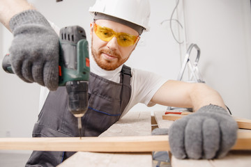 Worker man carpenter screws metal into wooden board with electric screwdriver