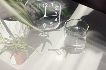 Fish collagen peptides powder and glass of water. alarm clock near spoon with collagen.