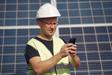 Engineer in a white helmet. Man near solar panel. Worker with a phone.