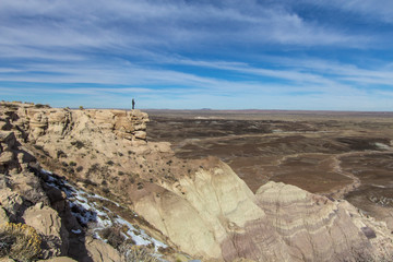 Standing On The Edge. Silhouette of a man standing on the edge of a steep canyon wall overlooking the vast barren desert below 