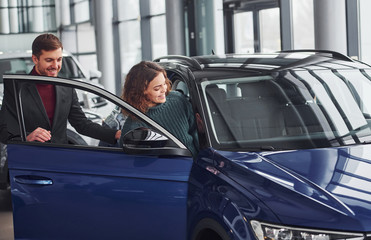 Fototapeta na wymiar Professional salesman assisting young girl by choosing new modern automobile indoors
