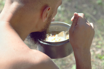a man with a beard eats soup from a pot. tourist enjoys food outdoors in the afternoon