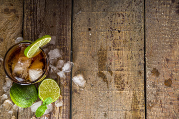 Summer iced alcohol drink with cola and lime. Rum and cola Cuba Libre cocktail. One long glass on wooden background copy space