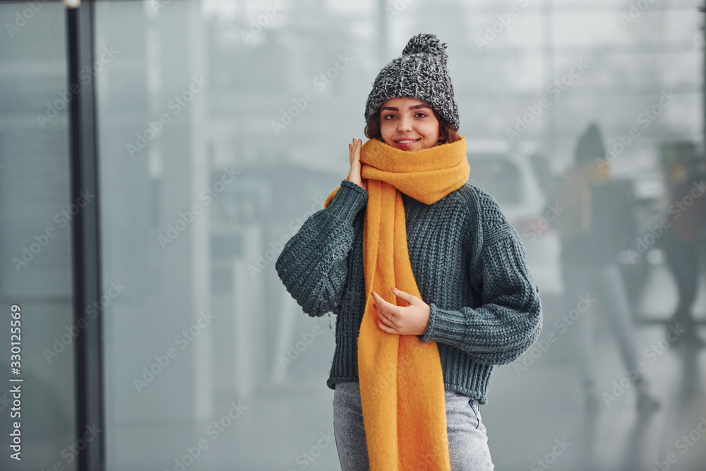 Wall mural Beautiful cheerful girl in yellow scarf and in warm clothes standing indoors against background with reflections