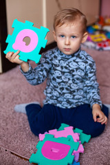 Little boy collects the puzzle sitting on floor. Big ABC squishy foam puzzle. Learning alphabet with puzzle mat
