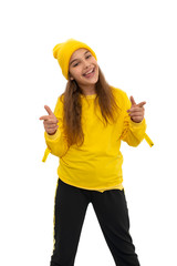 A young smiling girl teeneger wearing yellow tracksuit and knitted hat gesticults with hands expressing joy, isolated