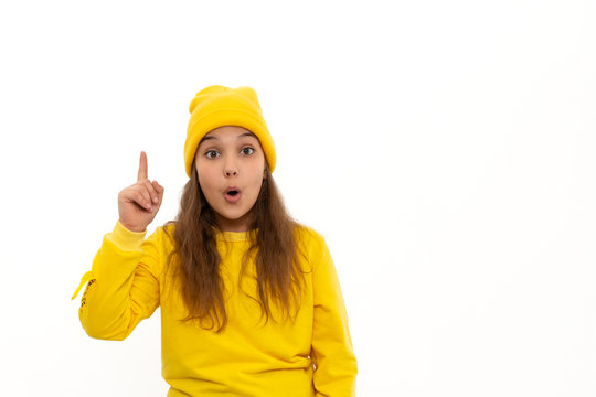 A young  girl teeneger wearing yellow hoody and knitted hat  proves something by raising his index finger up, isolated
