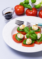 White Plate of Classic Italian Caprese Salad Ripe Tomatoes Fresh Basil Leaf Salad and Ingredients Vertical