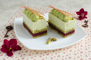 Contemporary cherry and pistachio mousse cakes decorated with red flowers on white plate on light background