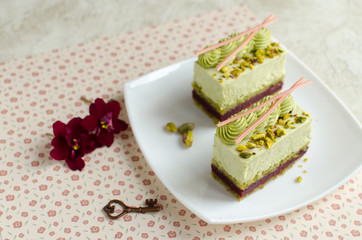 Contemporary cherry and pistachio mousse cakes decorated with red flowers on white plate on light background