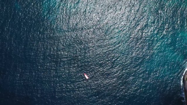 Top view from above boat anchored yacht floating in ocean runabout or cruiser stands in azure sea waters with coral reef visible. Weekender from drone beautiful weather with calm sea and sun shining