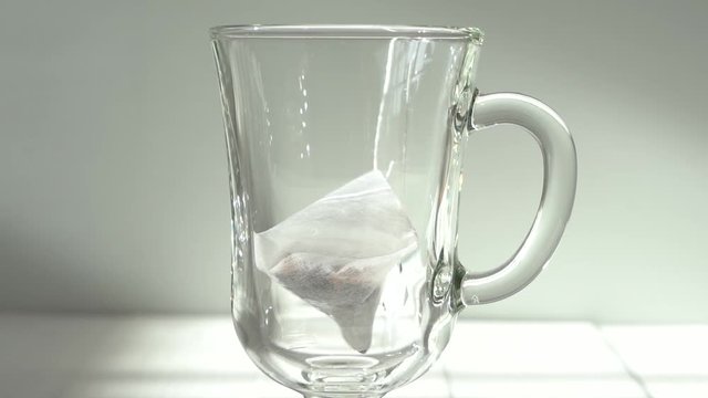 Closeup view of glass with white triangle package of fruit tea. Pouring hot water inside of cup.