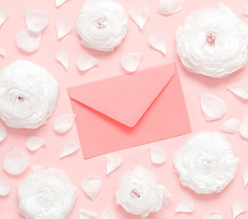 Obraz na płótnie Canvas Cream ranunculus flowers and envelope on a light pink background