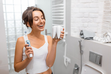 Portrait of a young and cheerful woman standing with electric toothbrush during morning hygiene procedures in the bathroom