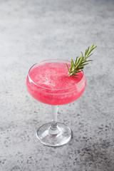 Glass of sparkling rose wine with shimmer edible glitter garnish rosemary on grey . Vertical format.