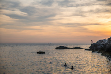 Silhouettes of unrecognizable people in the water and on the rocks by the sea.