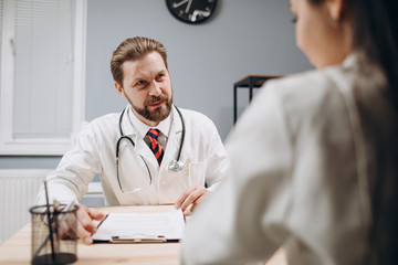 Cheerful senior medical employee sitting at a desk and listening to female intern's report